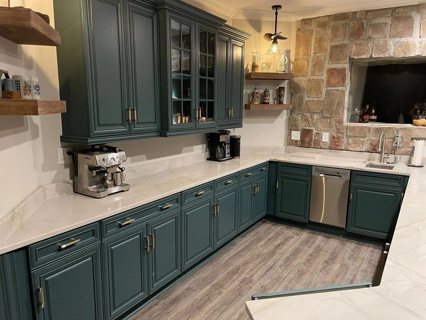 Deep green cabinetry with stone wall and floating wood shelves